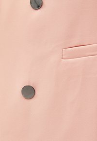 Ljusrosa tyg med en slät textur som har en enda svart knapp och en liten, infälld ficka på vänster sida.