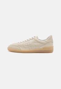 Beige lærstøvlett med rund tå, perforert design og lys beige gummisåle. Den har hvite snørebånd og en polstret krage.