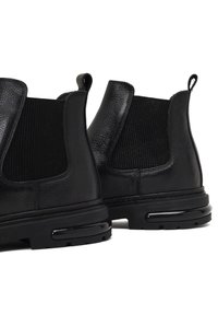 Botas Chelsea de cuero negro con paneles laterales elásticos y suelas de goma. Presentan una textura suave, punta redondeada y bucles para facilitar el calzado.