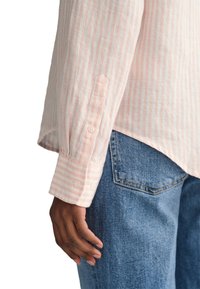 Hellrosa und weiß gestreiftes Langarmhemd mit geknöpften Manschetten, kombiniert mit blauer Denim. Weicher Stoff, lockere Passform und abgerundeter Saum.