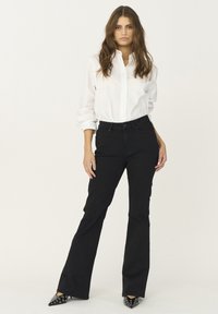 Jeans negre evazați asortați cu o cămașă albă cu nasturi. Cămașa are mâneci răsucite, iar ținuta este completată de tocuri negre ascuțite cu accente argintii.