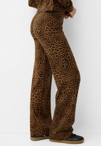 Kalhoty s leopardím potiskem v hnědé a černé barvě, vyrobené z měkké tkaniny. Mají vysoký pas a volný střih, doplněné černými teniskami.