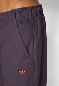 Σκούρο μοβ παντελόνι με ελαστική μέση και ομαλή υφή. Διαθέτει πλαϊνές τσέπες και κεντημένο κόκκινο λογότυπο στον αριστερό γοφό.