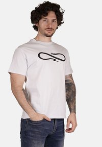 T-shirt bianca in cotone con una stampa di un serpente nero a forma di simbolo dell'infinito, maniche corte e colletto tondo.