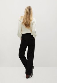 Biały sweter z prążkowanym wzorem i czarne, szerokie spodnie. Spodnie mają tylne kieszenie. Modelka ma długie, falowane włosy i stoi na neutralnym tle.