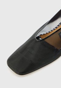 Chaussure plate noire avec un bout carré, fabriquée dans un matériau texturé, dotée de panneaux latéraux en mesh et d'une doublure intérieure à motif.