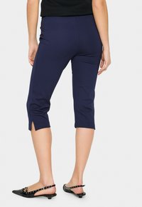 Navy capri pants with side slits at the hem, made from stretchy fabric, featuring a fitted design and an elastic waistband.