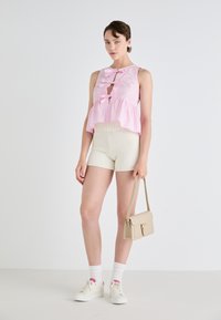 Roze en witte gestreepte mouwloze top met drie strikken aan de voorkant, gecombineerd met crèmekleurige gebreide shorts en witte sneakers, terwijl ze een beige tas vasthoudt.