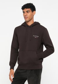 Καφέ φούτερ με κουκούλα και μπροστινή τσέπη, με λευκό κεντημένο λογότυπο "HILFIGER". Φτιαγμένο από μείγμα βαμβακιού, διαθέτει ριμπ μανσέτες και στρίφωμα.