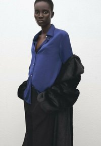 Royal blue silk shirt with a collar and buttons, layered under a black faux fur coat. The coat features a soft, plush texture and dramatic shape.