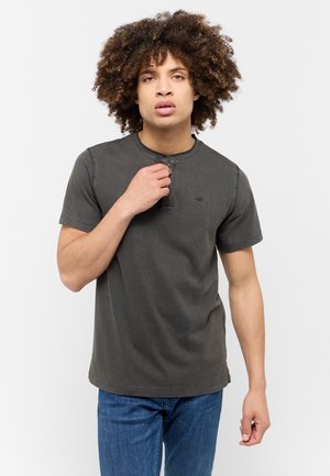 T-shirt grigio scuro a maniche corte con scollatura rotonda e dettaglio a bottoni al colletto. Materiale in cotone con leggera texture. Indossato con jeans blu.