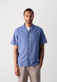 Camicia azzurra a maniche corte con bottoni realizzata in tessuto leggero, presenta un colletto a camicia, bottoni frontali e una texture sottile.