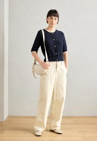 Navy knitted cardigan with short sleeves and button closure, paired with cream-colored wide-leg pants and a small cream shoulder bag.