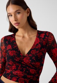 Czarny długi rękaw top z czerwonym wzorem kwiatowym, głęboki dekolt w serek i marszczona faktura w talii. Miękki, lekki materiał.