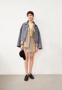 Jeansjack, beige gestreepte blazer over bijpassende rok, gele top, zwarte schoenen en pet. Heeft knopen op de blazer en een relaxte pasvorm.