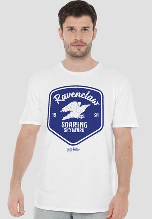 Mann trägt weißes T-Shirt mit blauem Ravenclaw-Emblem, Vogeldruck und Text "Soaring Skyward 1991" aus der Harry-Potter-Serie.