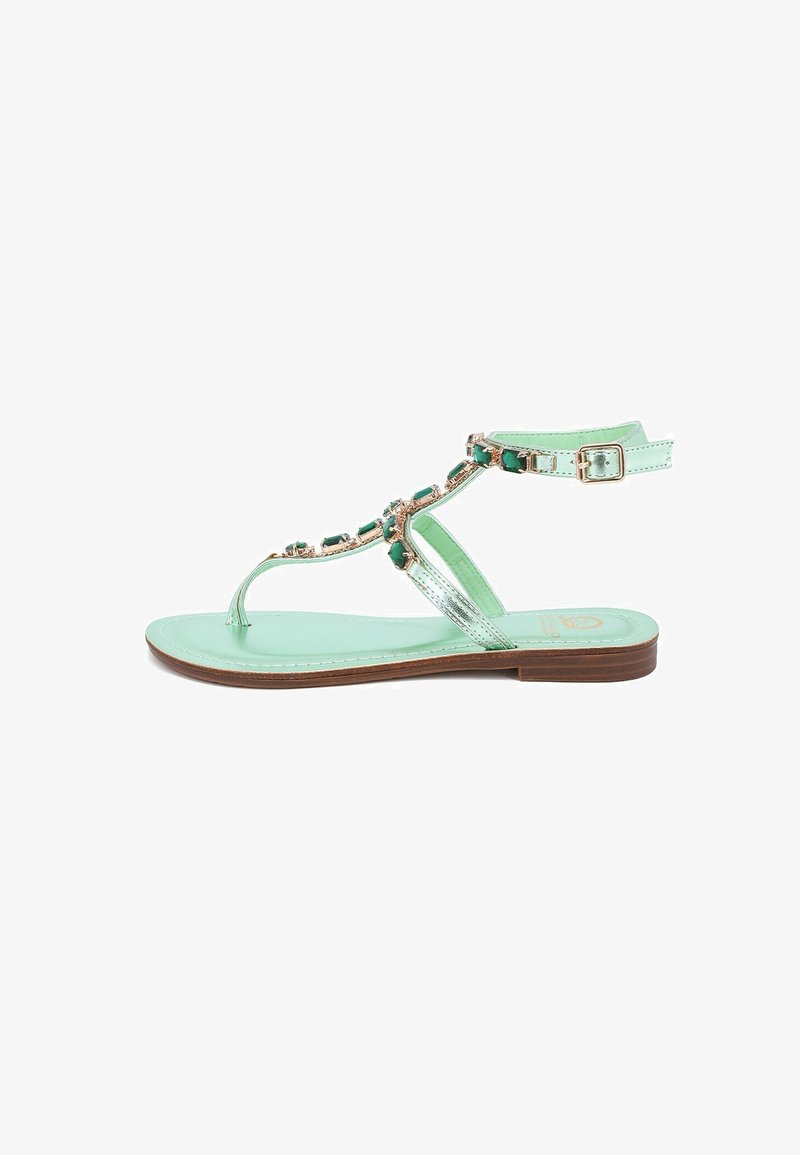 Sandal in verde menta con suola piatta, cinturini metallici e pietre decorative verdi lungo la parte superiore. Include una cinghia regolabile alla caviglia.