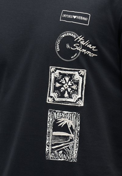 Μαύρο ύφασμα με λευκά λογότυπα Emporio Armani, συμπεριλαμβανομένων κυκλικών, ορθογώνιων και χειρόγραφου στυλ κειμένου με διακοσμητικά σχέδια και έναν φοίνικα.