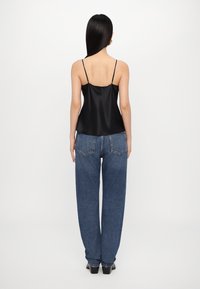 Svart satin-camisole med tynne stropper, kombinert med høyt liv blå denim jeans med avslappet passform og store baklommer.
