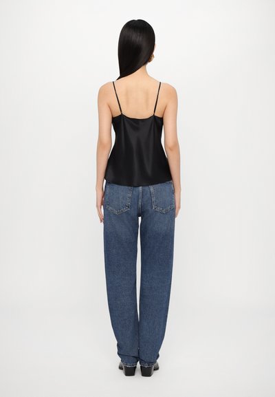 Camisola din satin negru cu bretele subțiri, asortată cu blugi din denim albastru cu talie înaltă, având o croială lejeră și buzunare mari pe spate.