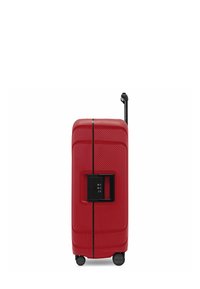 Valigia rigida rossa con superficie texture, cerniera nera centrale, chiusura integrata, manico estraibile e quattro ruote per la mobilità.