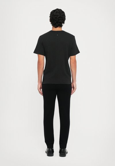 Camisa negra de corte relajado, con mangas cortas y detalle en la costura trasera, combinada con pantalones negros ajustados y zapatos negros.