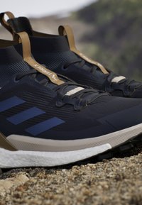 Dunkelblaue Sportschuhe mit einer strukturierten Oberseite, hellbraunen Akzenten, weißer Sohle und drei blauen Streifen an der Seite. Verfügt über integrierte Schnürung.