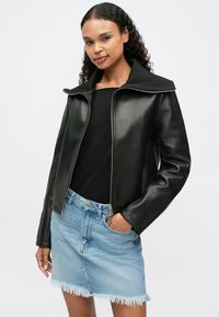 Μαύρο δερμάτινο μπουφάν με φερμουάρ μπροστά και φαρδύ γιακά. Φορεμένο πάνω από ένα μαύρο μπλουζάκι και ανοιχτόχρωμο μπλε τζιν φούστα με ξηλωμένη άκρη.