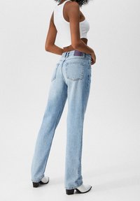 Vaqueros de tiro alto en azul claro con un ajuste relajado, que presentan bolsillos traseros y una etiqueta morada en la cinturilla. Textura de denim suave.