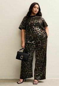 Tweedelige set met luipaardprint in donkere tinten, bestaande uit een losse top met korte mouwen en wijde broek. Zwarte handtas met gouden hardware.