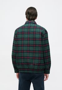 Πράσινο καρό σακάκι με κόκκινες και ναυτικές λεπτομέρειες, διαθέτοντας γιακά, μακριά μανίκια και ελαστικούς καρπούς. Κατασκευασμένο από υφασμάτινη φλάνελ.