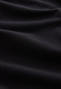 Gros plan d'un tissu lisse, noir foncé avec de doux plis et une texture souple.