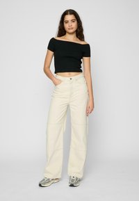 Černý crop top bez ramínek kombinovaný s krémovými širokými kalhotami; má vysoký pas, přední kapsy a vyšívané detaily. Celkový look doplňují tenisky.