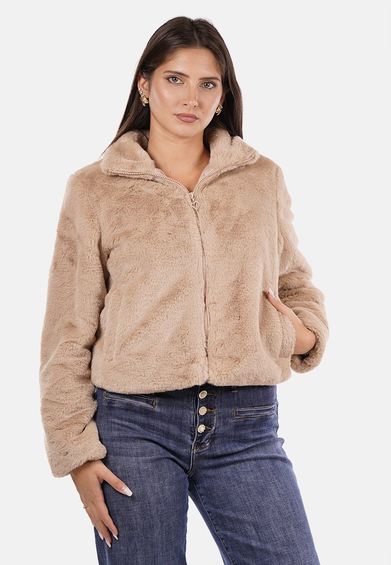 Giacca in finta pelliccia, con zip, di colore beige chiaro, design cropped con colletto alto, texture morbida e spalle cadenti. Indossata con jeans blu scuro.