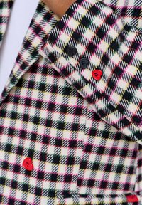 Kostkovaná rukávová bunda s růžovými, černými, zelenými a žlutými kostkami, která má dva černé a jeden červený knoflík ve tvaru srdce.