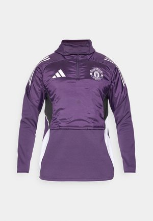 Fialový pulóver s polovičným zipsom z lesklého materiálu, s čiernymi bočnými panelmi, bielymi akcentmi a logom Manchester United na hrudi. Mäkká textúra.