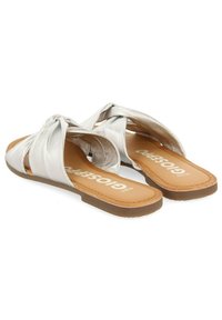 Sandalias metálicas plateadas con diseño de nudos cruzados, textura suave, suela plana y plantilla marrón con nombre de la marca impreso.