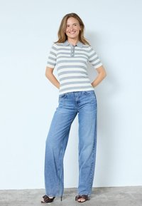 Prugasta polo majica kratkih rukava u sivoj i bijeloj boji, kombinirana s visokim strukom, širokim nogavicama svijetloplavih traperica i smeđim sandalama na petu.