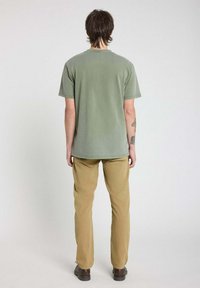 T-shirt vert olive à manches courtes associé à un pantalon slim beige. Le haut présente un col rond et une coupe décontractée.