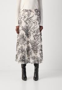 Vrouw in een geplisseerde midi-jurk met een zwart-wit stadsuitzichtprint, gecombineerd met zwarte puntige laarzen en een lange mouw witte top.