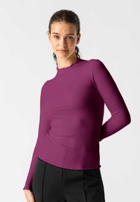 Dlouhý rukáv top v tmavě purpurové ribbové látce s okrajem a lemem ve vlnkovaném stylu. Stylizováno s černými kalhotami s vysokým pasem.