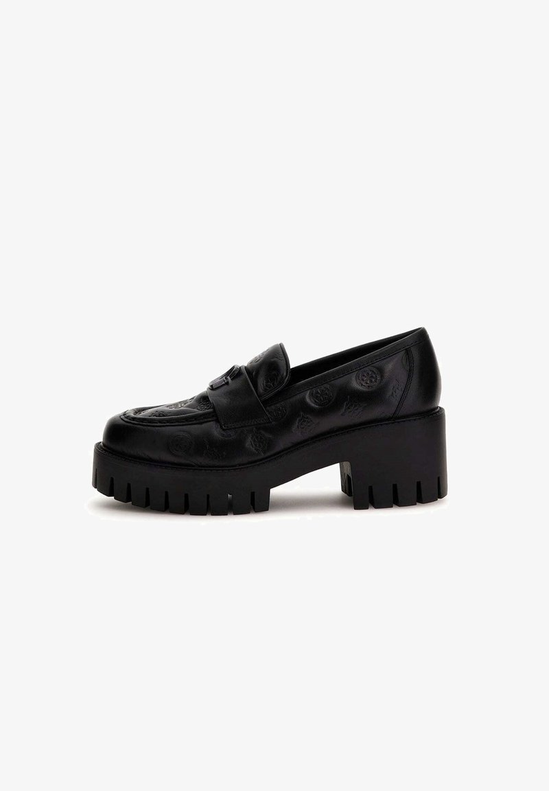 Mocassin en cuir noir avec semelle à crampons épaisse et talon bloc, motifs circulaires embossés, et une large bride sur le dessus.