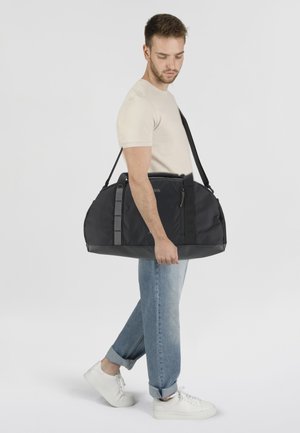 Borsone nero con accenti grigi, forma rettangolare e molteplici scomparti con zip. Realizzato in tessuto resistente, portato con una tracolla.