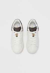 Beli športni copati z rjavim tkanim manšetom z teksturo, z zlatim logotipom in belimi vezalkami, z gladkim usnjenim zgornjim delom in gumijastim podplatom.