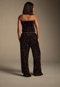 Sort paliettoverdel to-delt sæt med en stropløs top og løstsiddende bukser med elastik i taljen, der skaber en tekstureret, glitrende effekt.