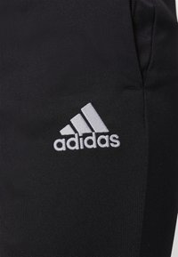 Tissu noir avec logo Adidas brodé en blanc présentant trois bandes diagonales et le nom de la marque.