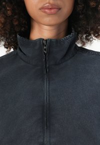 Black zip-up jacket featuring a high collar, smooth texture, and seam detailing. The zipper is centrally located with a matte finish.