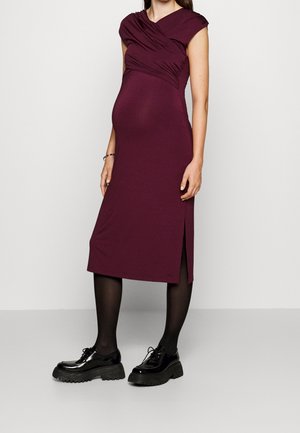 Syvä bordeauxvärinen äitiysmekko, jossa on istuva siluetti, lyhyet hihat ja laskostettu yksityiskohta. Sivuhalkio ja sileä kangas. Yhdistetty mustiin kenkiin.