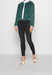 Tealfärgad kort faux fur-jacka med kanalstygn, i kombination med svarta slim fit-jeans och vita knutna klacksandaler.