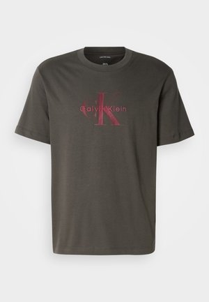 Dunkelgrünes Baumwoll-T-Shirt mit kurzen Ärmeln. Mit einem großen, verblassten roten Calvin Klein Logo in der Mitte der Vorderseite. Klassische Rundhalsgestaltung.